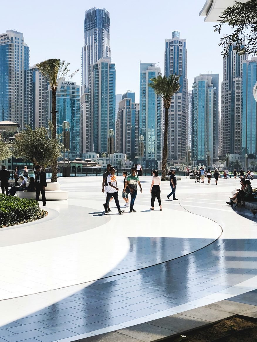 Dubai property investment – modern Dubai skyline of high-rise towers behind a palm-lined pedestrian plaza in daylight for article on if can foreigners buy property and live in Dubai.