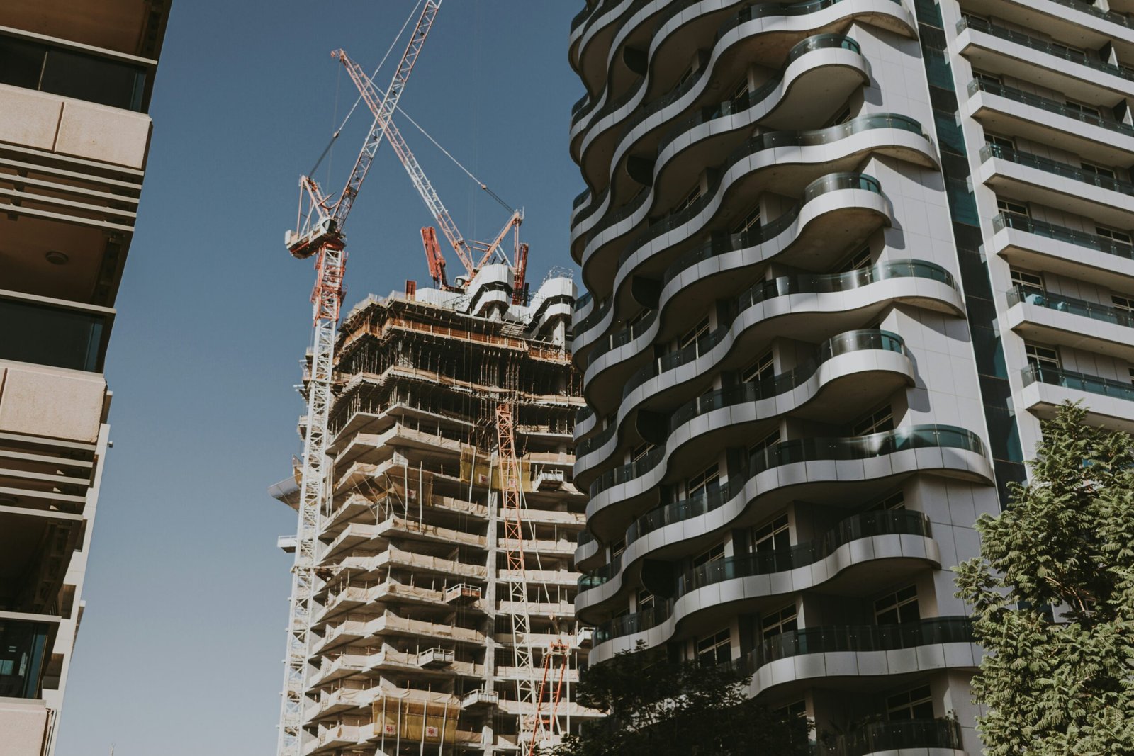 High-rise residential building under construction in Dubai, with cranes and neighbouring completed apartment towers.