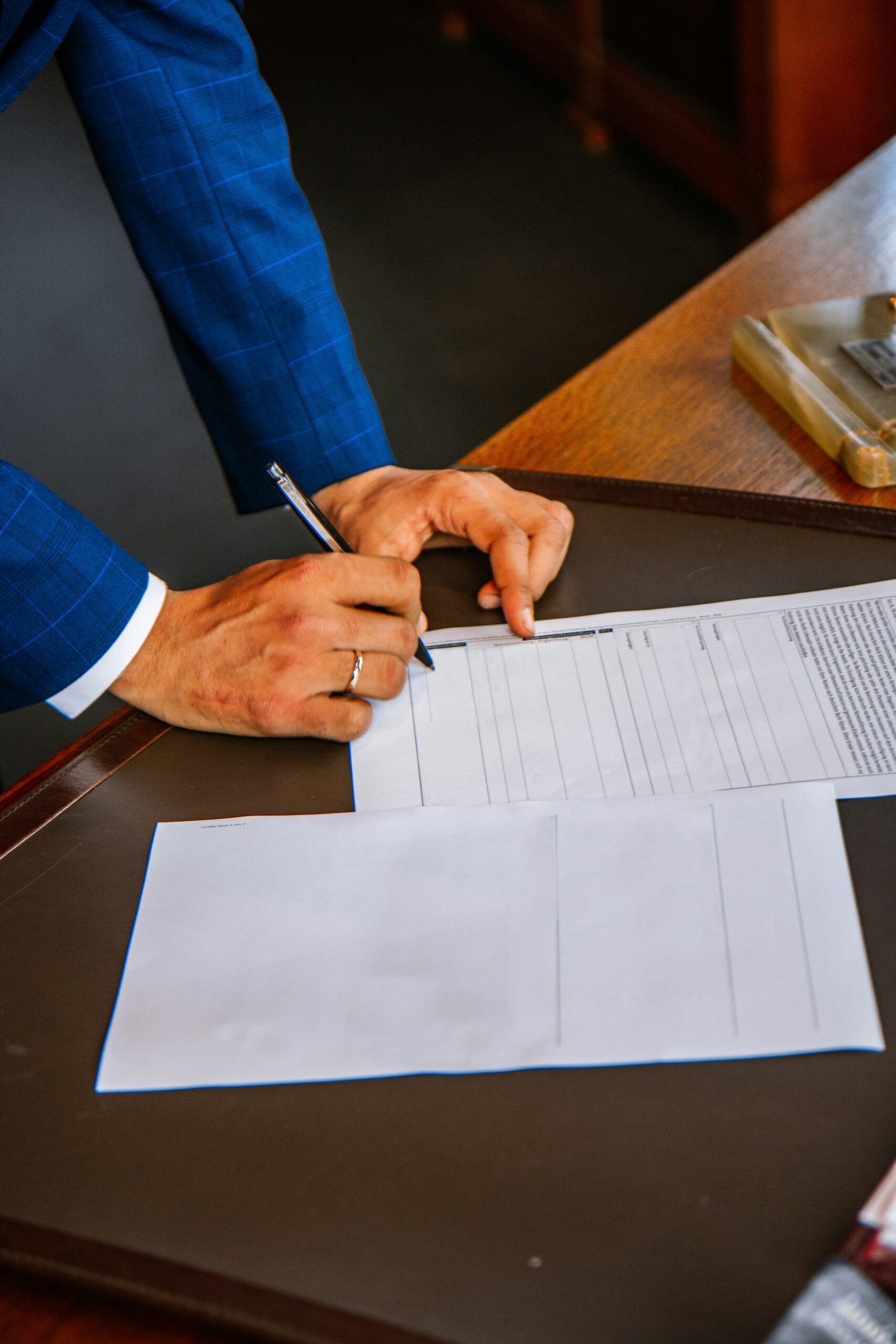 Person signing a rental or property agreement at a desk, with documents laid out and a pen in hand.