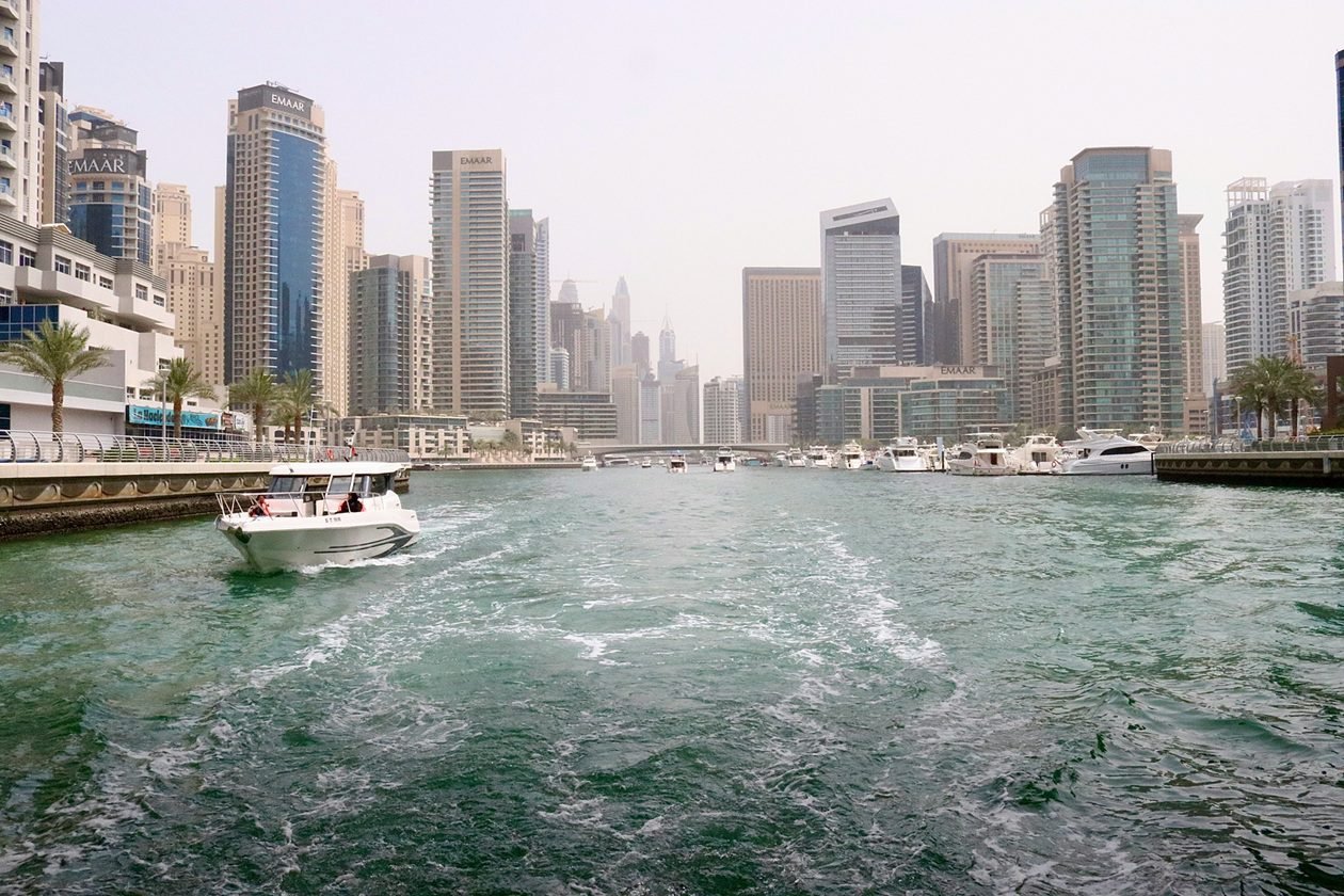 Boat cruising through Dubai Marina canal with high-rise residential towers and waterfront skyline, illustrating How Much Money Do You Need to Invest in Dubai article across established property districts.