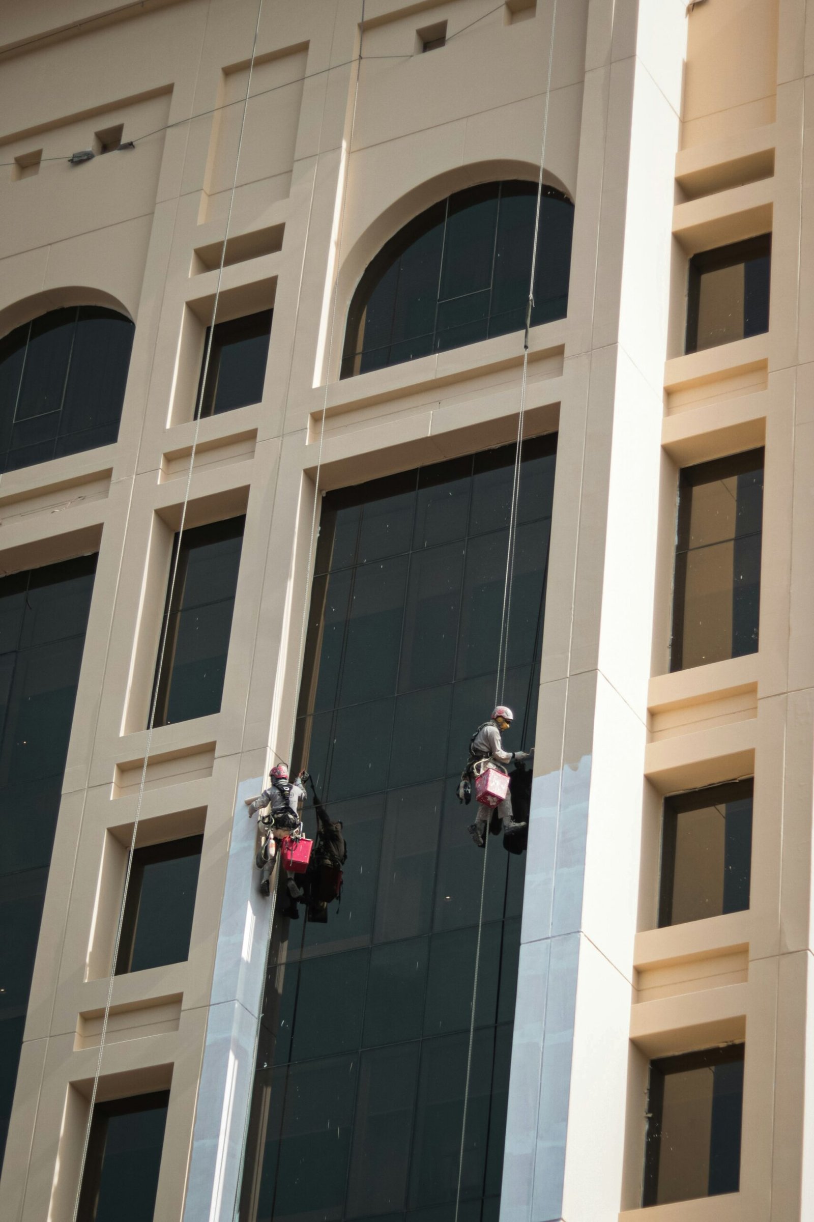 Building maintenance workers suspended by ropes cleaning the exterior glass façade of a high-rise building in Dubai.