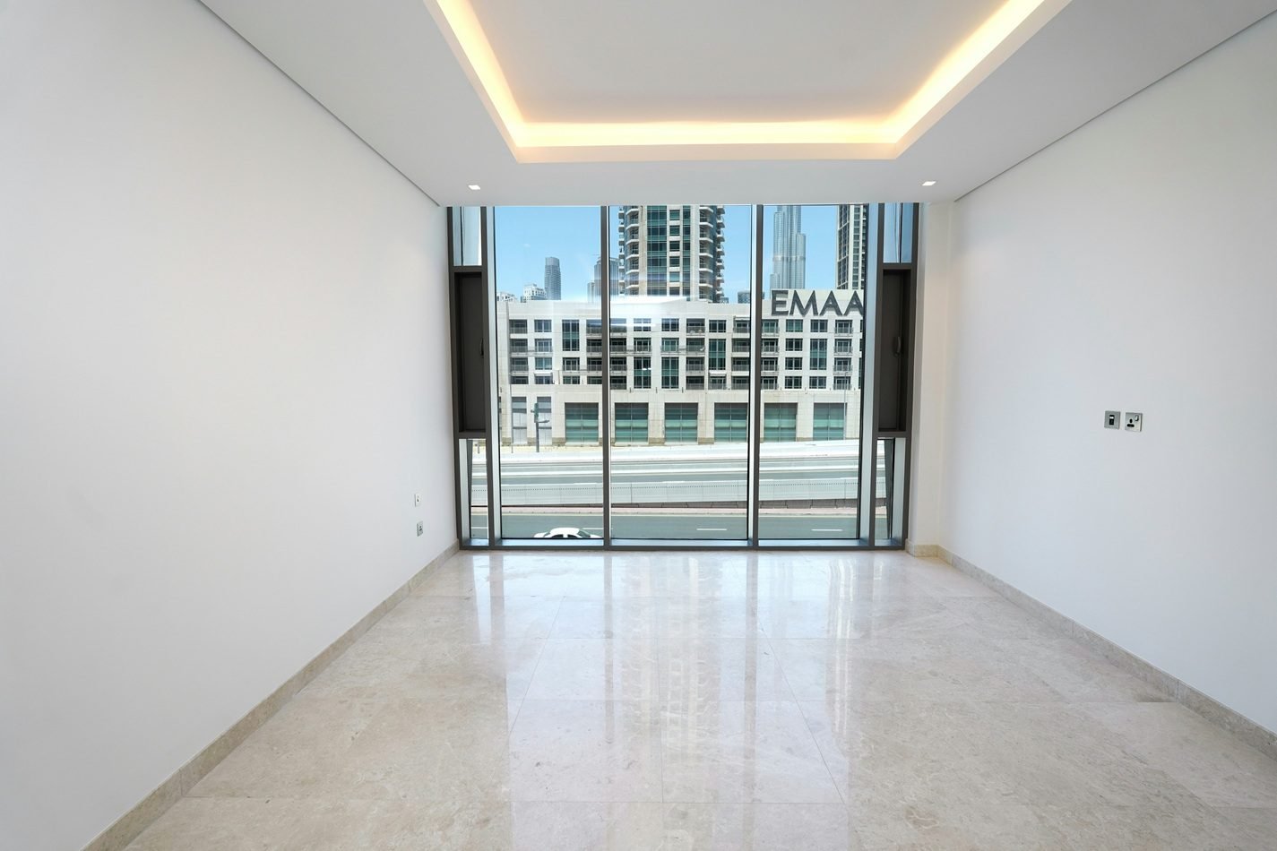 Buy an apartment in dubai – empty modern apartment living room with floor-to-ceiling windows overlooking Downtown Dubai buildings.